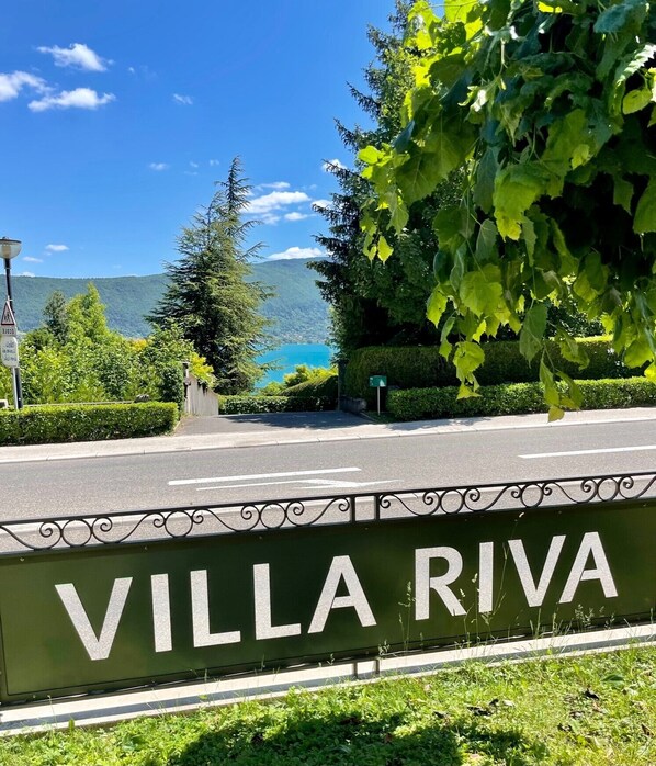 Een bord met de tekst 'VILLA RIVA', met zicht op een meer en bergen op de achtergrond.