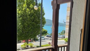 A balcony with a wicker chair, a table, and a view of a street with cars and a tree. - Villa Riva (Veyrier-du-Lac)