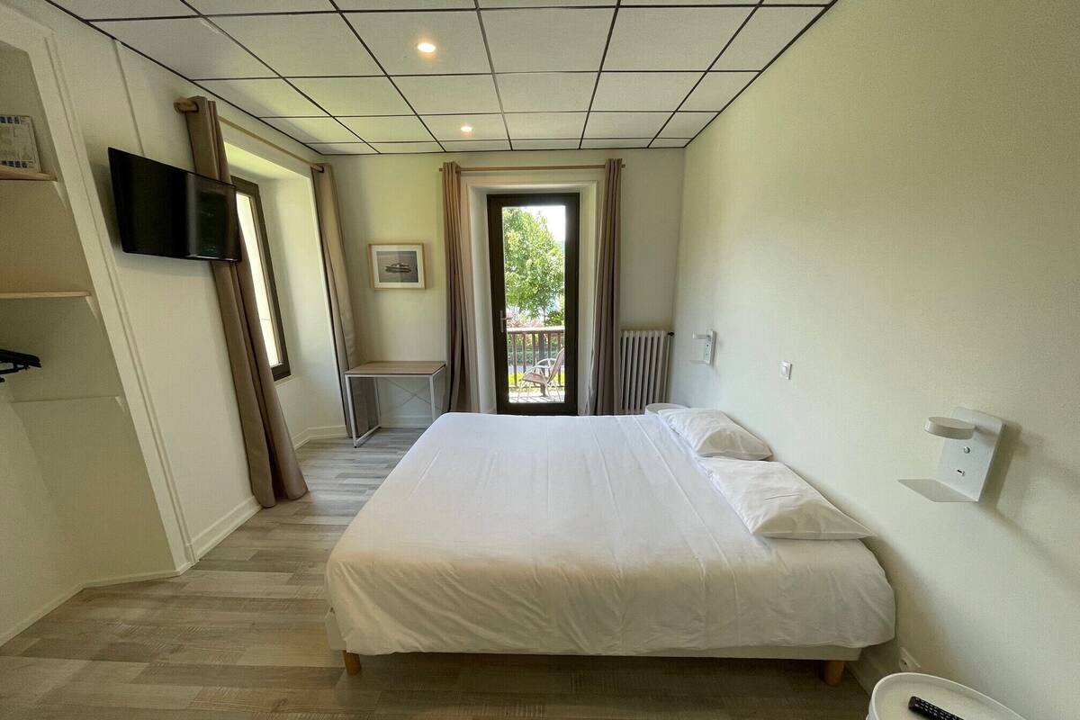 Une chambre d’hôtel avec un lit, un téléviseur fixé au mur, une petite table et une fenêtre avec des rideaux.
