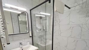 A modern bathroom with a marble backsplash, a glass-enclosed shower, a white sink, and a wooden vanity. - Villa Riva (Veyrier-du-Lac)