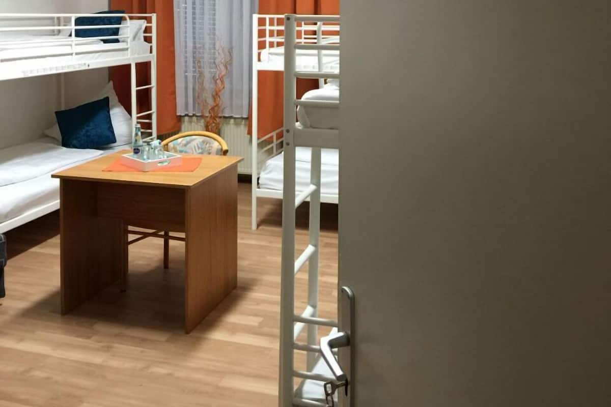Asuntolan huone, jossa on kerrossängyt, puinen pöytä ja pieni työpöytä.