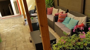 Un porche cubierto con mobiliario de mimbre, un pilar de madera y plantas en macetas.
