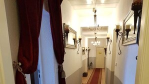 Un pasillo con alfombra roja, apliques en la pared y un candelabro.
