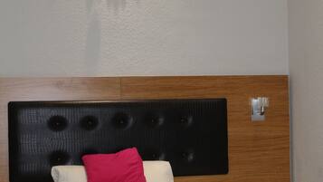 A neatly made bed with white bedding and a single red pillow, a wooden headboard, and a wall-mounted decorative mirror.