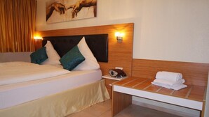 Una habitación de hotel con una cama grande, una mesita de noche con una radio y una lámpara fijada a la pared.