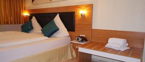A hotel room with a large bed, a bedside table with a radio, and a wall-mounted light.