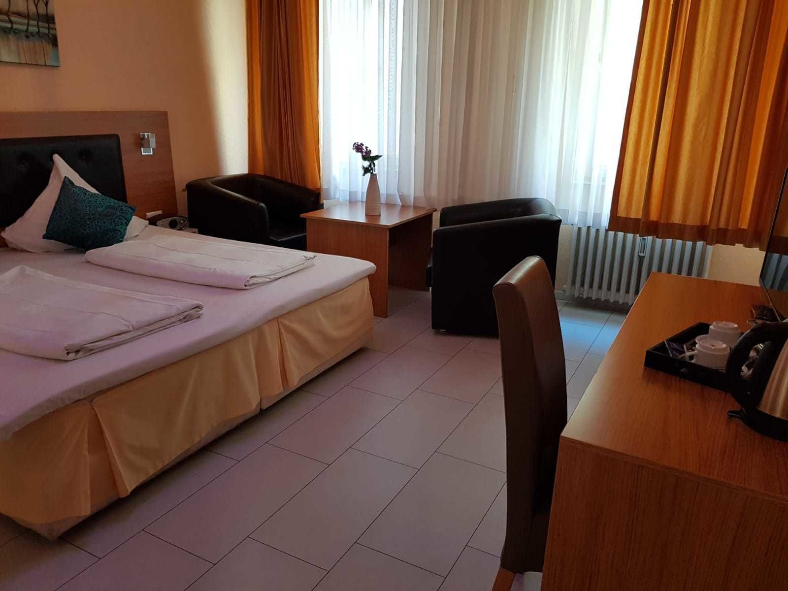 A hotel room with a bed, a desk, a chair, a small table, and a window with curtains.