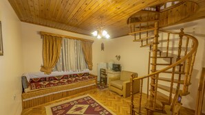 Une pièce avec un escalier en colimaçon en bois, un lit recouvert d’une couvre-lit à motifs, un petit canapé et un plancher en bois.