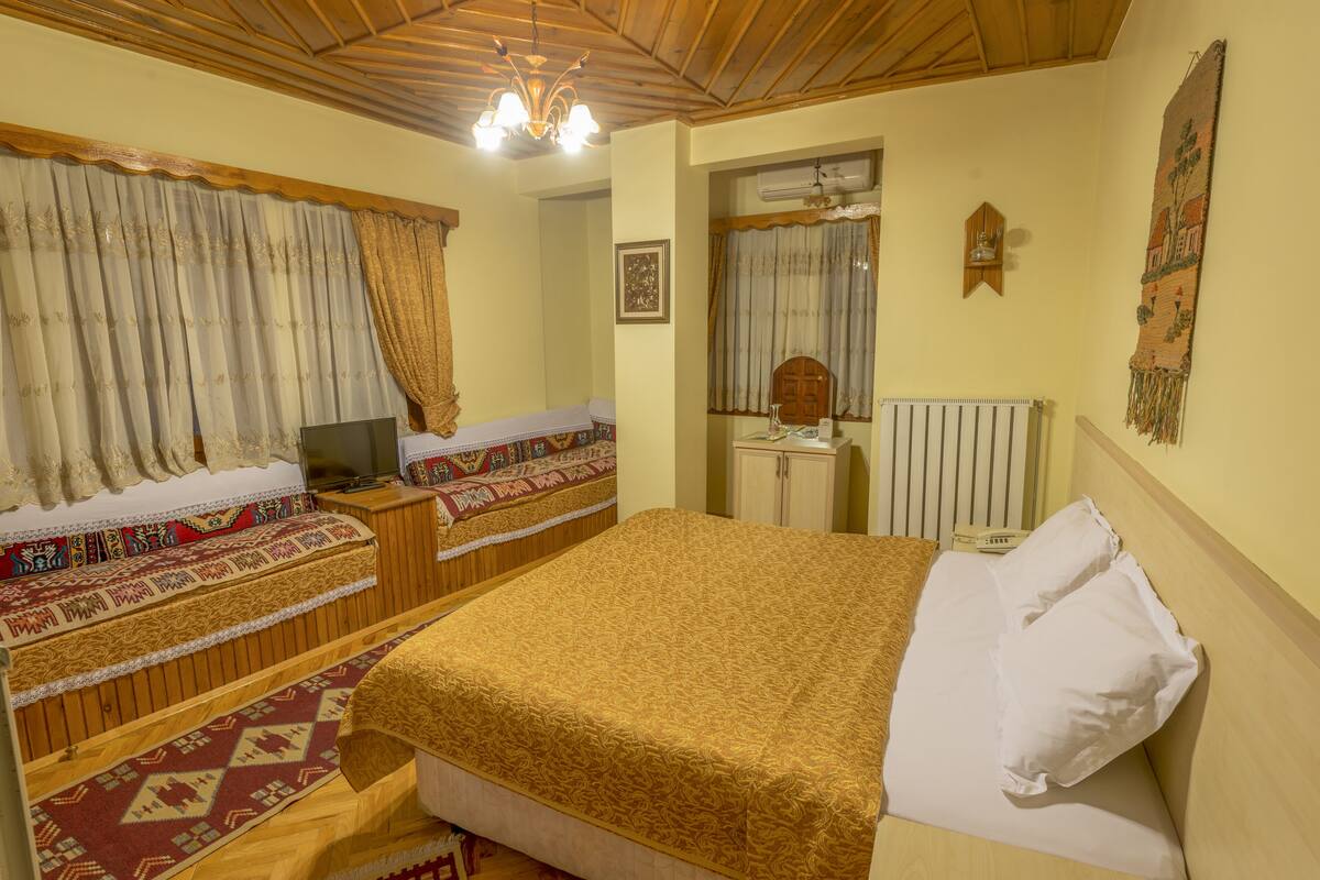 Een kamer met een bed, een bureau, een stoel, een televisie en een raam met gordijnen.