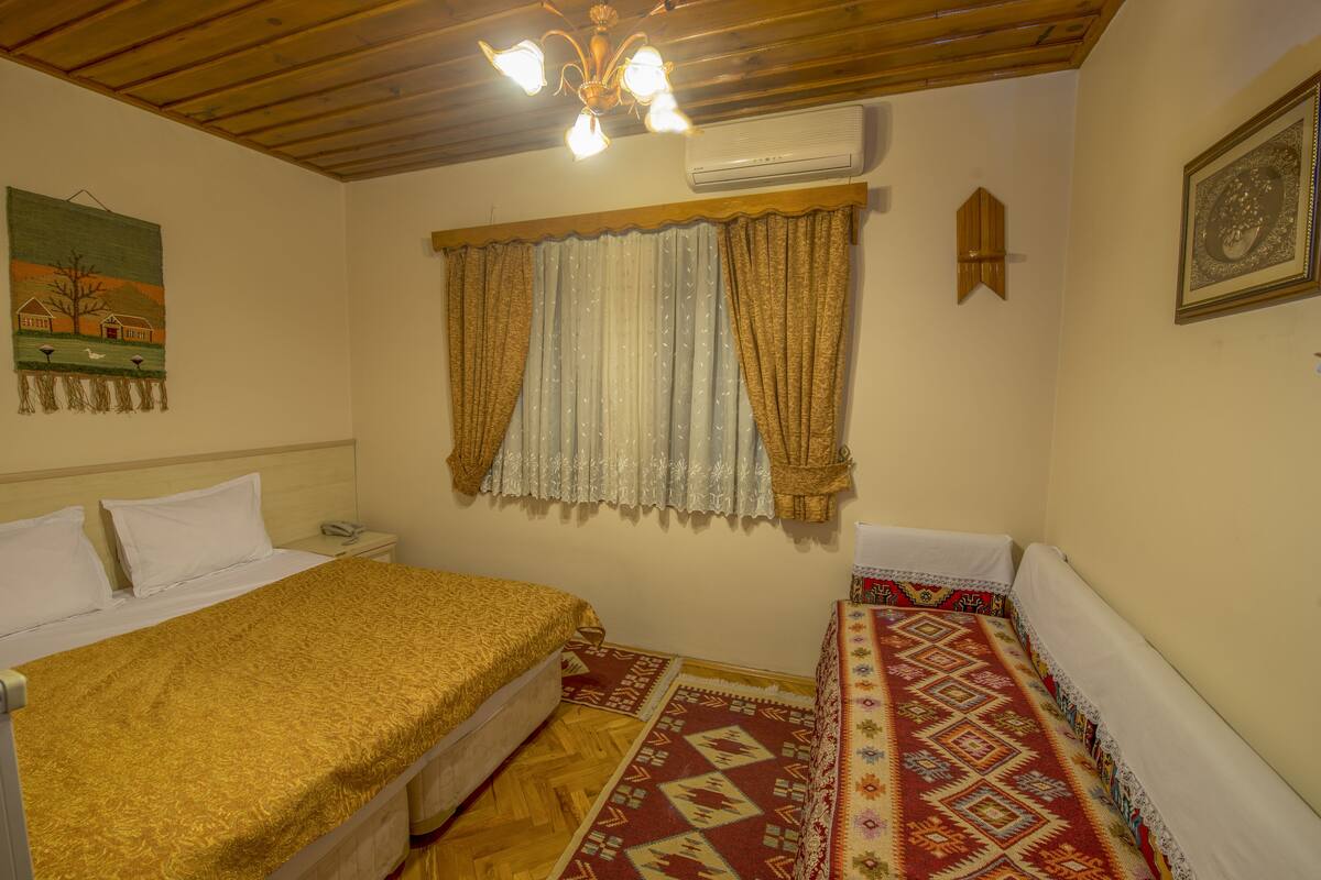Een slaapkamer met een bed, nachtkastje, wandairconditioning en een raam met gordijnen.