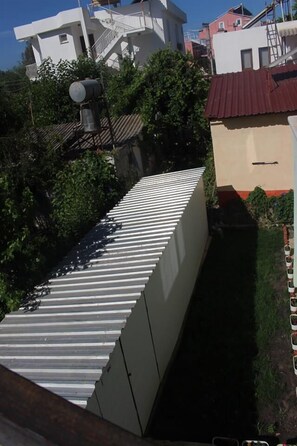A rooftop with a corrugated metal roof, surrounded by greenery and adjacent buildings. - Sirin Pansiyon (Fethiye)