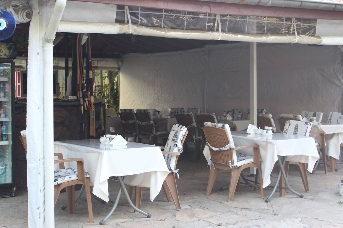An outdoor dining area with tables and chairs, covered by a canopy.