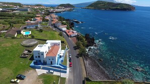 An aerial view of a coastal town with a prominent mountain in the background, clear blue waters, and a mix of residential and commercial buildings along the shoreline. - Lofts Azul Pastel (Horta)