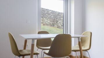 A dining area with a white table and four chairs, a stone wall visible through a window, and wooden flooring.