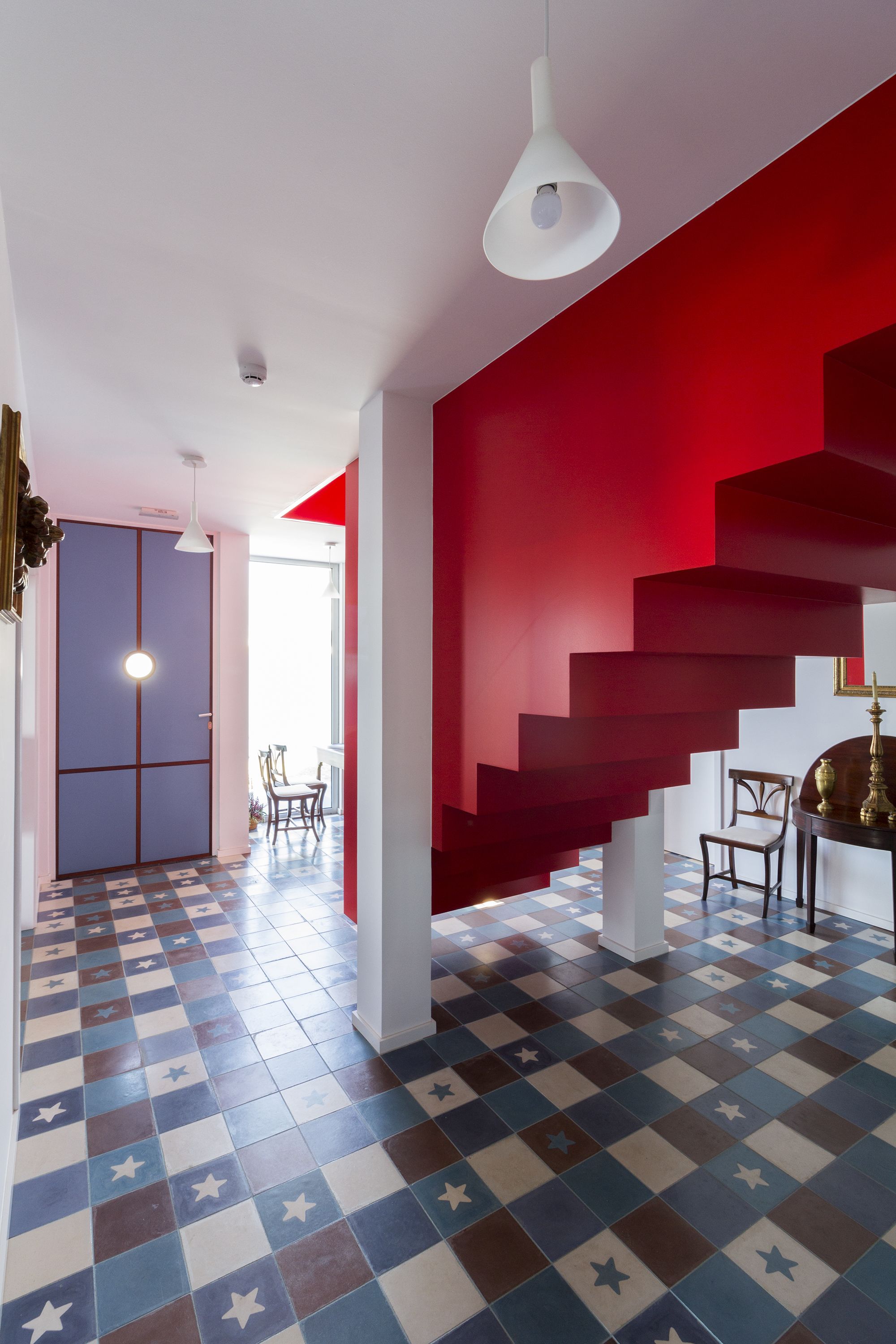 Ein modernes Interieur mit einem Schachbrettfußboden, einer roten Treppe und einer Pendelleuchte.