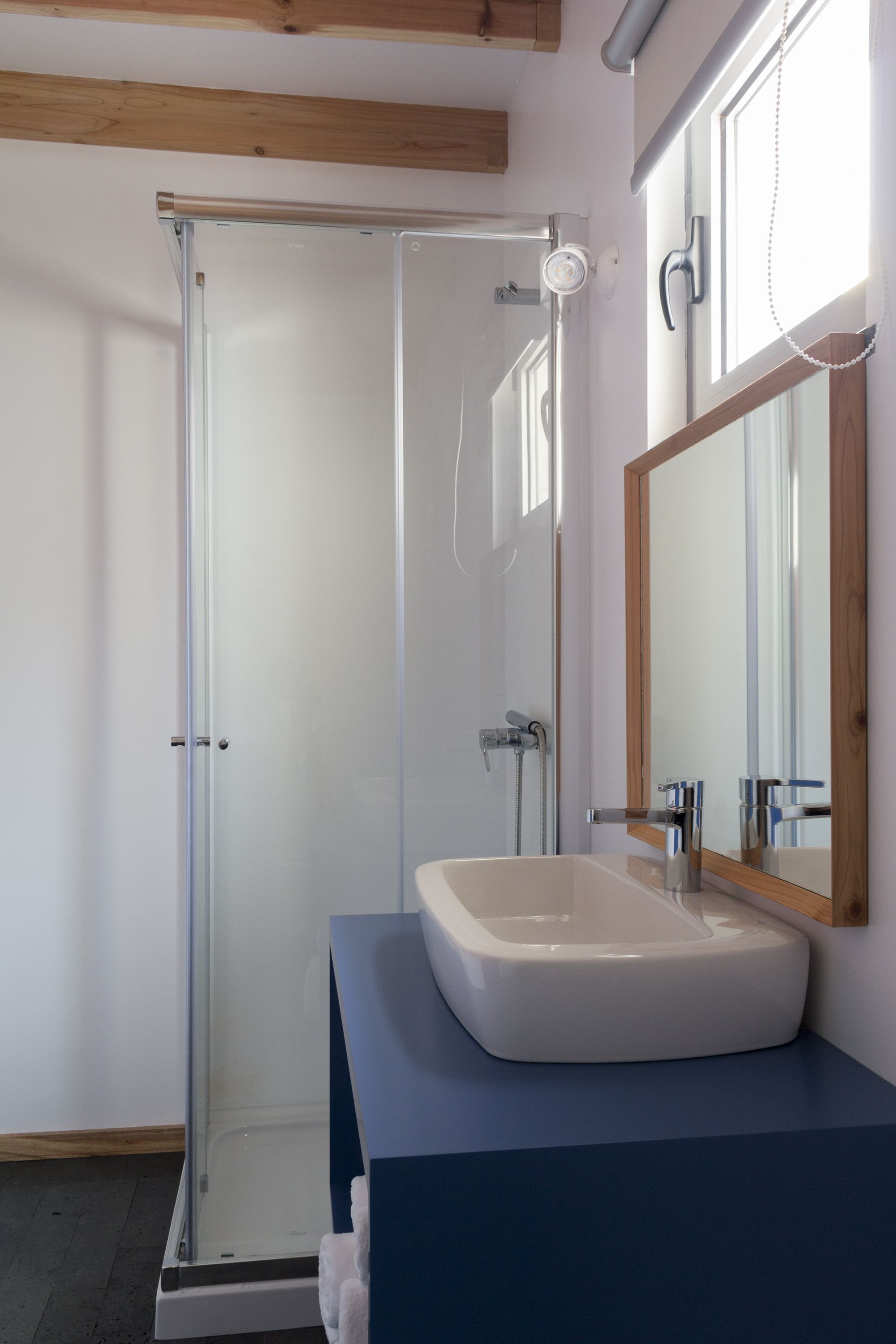 Une salle de bain moderne avec une douche à parois de verre, un lavabo blanc et un miroir encadré en bois.