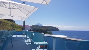 A terrace with blue chairs and white umbrellas overlooking the sea. - Lofts Azul Pastel (Horta)