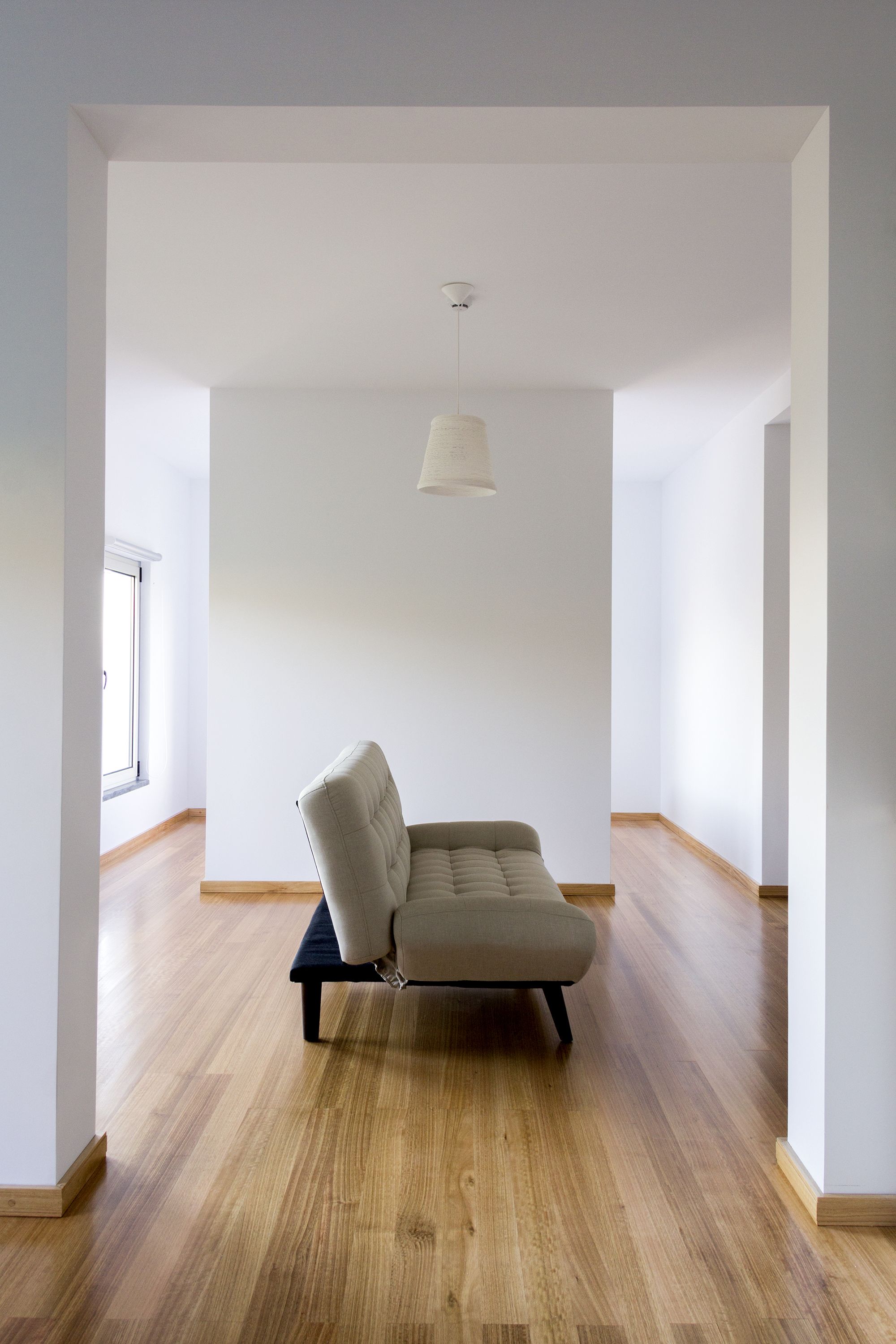 Una habitación amplia con un sofá de color claro, una lámpara colgante y suelo de madera.