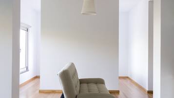 Een ruime kamer met een lichtkleurige bank, een hanglamp en houten vloeren.
