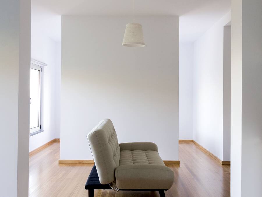 Una habitació àmplia amb un sofà de tons clars, una làmpada penjant i terres de fusta.