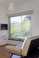 Una habitación con un amplio ventanal, un televisor de pantalla plana en la pared y un sillón acolchado.