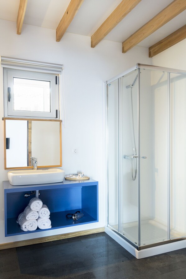 A modern bathroom with a glass-enclosed shower, a sink with a mirror above it, and a blue shelf with towels.
