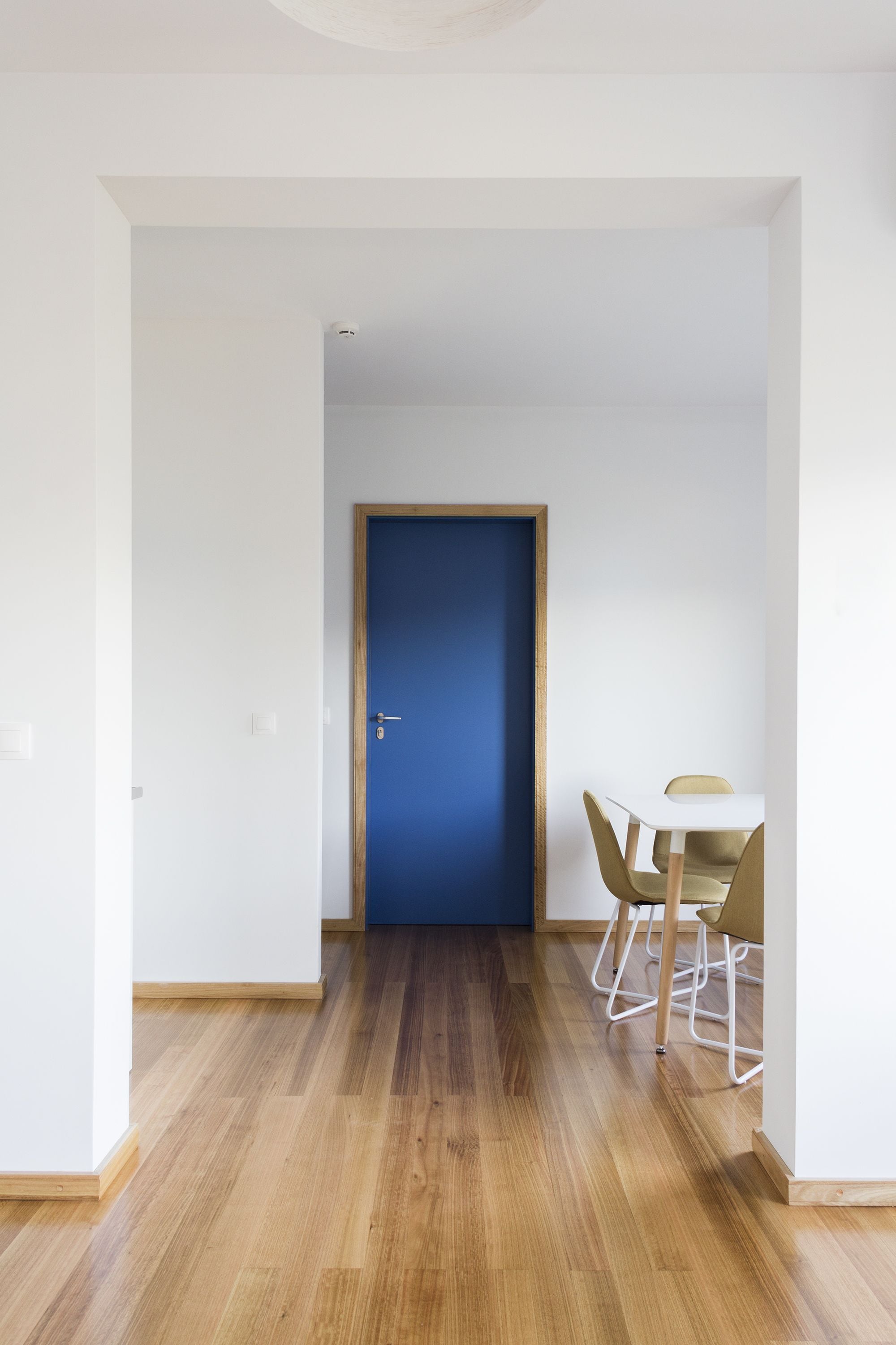 A hallway with a wooden floor, a blue door, and a white table with two chairs.