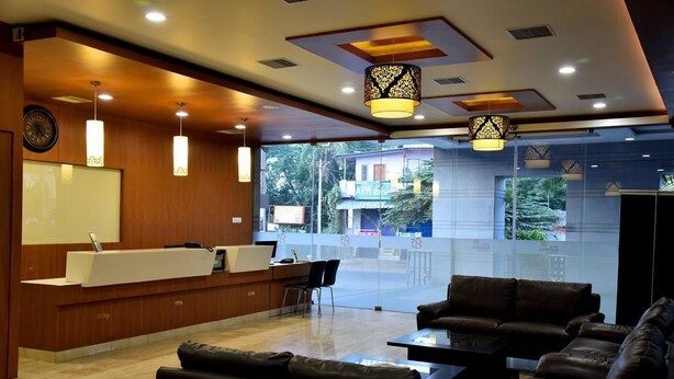 A modern reception area with a reception desk, seating area, and large windows offering a view of the outside. - Rathna Residency (Salem)