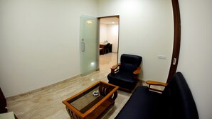 A living room with a glass door leading to a bathroom, a dark blue sofa, a wooden coffee table, and a wooden chair. - Rathna Residency (Salem)