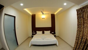 A hotel room with two beds, a ceiling fan, recessed lighting, a door, and a patterned curtain. - Rathna Residency (Salem)