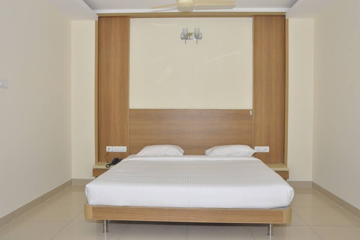 A modern bedroom with a wooden headboard, a bed with white bedding, and a bedside table with a phone.