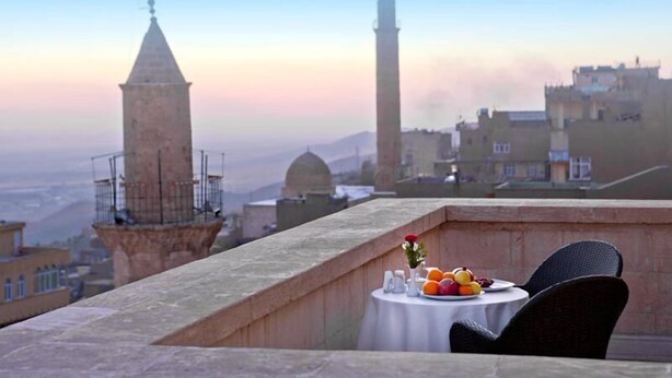 Une terrasse sur le toit, avec une table dressée pour le dîner, offrant une vue sur le paysage urbain, avec ses bâtiments historiques et son imposant minaret.
