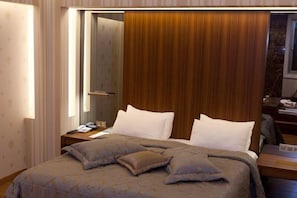 A hotel room with a large bed, a wooden headboard, a bedside table with a lamp, and a mirror. - Reyhani Kasri - Special Class (Mardin)