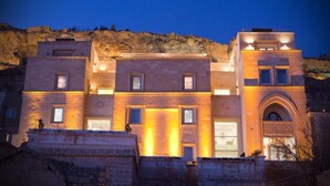 Un immeuble à plusieurs étages, doté d’une façade en pierre, de fenêtres illuminées et d’une entrée centrale surmontée d’une arche.
