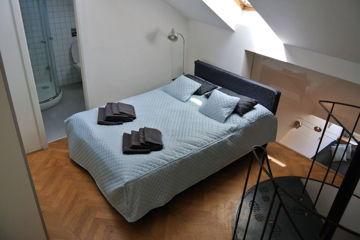 Un dormitorio con cama, mesita de noche, lámpara y vistas al baño.