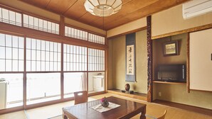 A traditional Japanese room with tatami flooring, a low wooden table, a TV mounted on the wall, and a sliding door leading to another room. - Tsukasaya Ryokan (Tsuruoka)