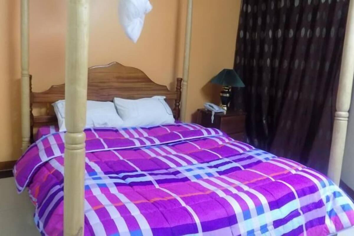 Una cama con cabecera de madera, colcha a rayas morada y blanca, y almohada blanca.