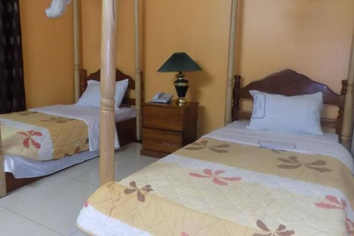 Una habitación con dos camas con dosel, mesitas de noche de madera, una lámpara y un teléfono.
