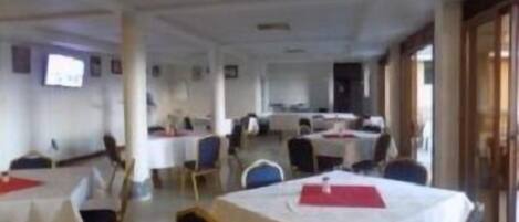 Un salón de conferencias amplio con varias mesas y sillas, paredes blancas y una puerta de madera.