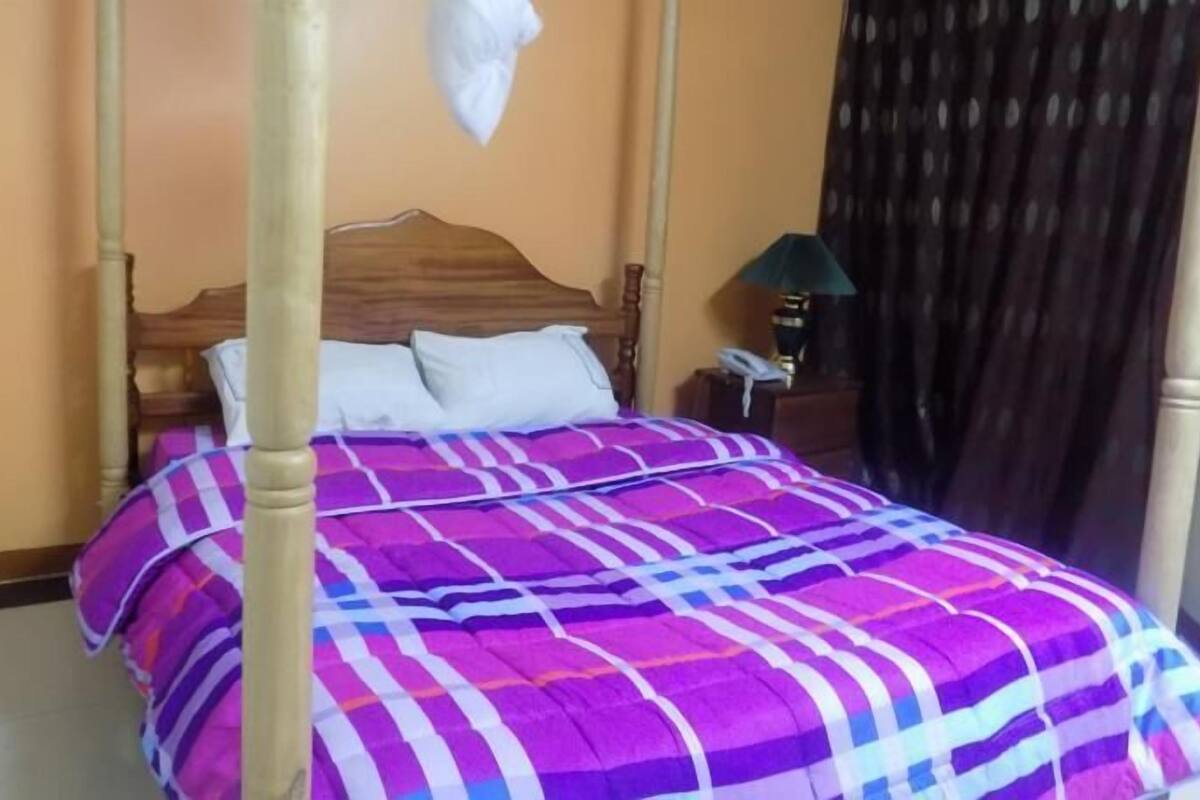Una cama con cabecera de madera, colcha a rayas morada y azul, y almohadas blancas.