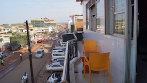 A balcony with yellow chairs, a view of a busy street with cars and motorcycles, and a building with large windows. - Sunrise Hotel (Kampala)