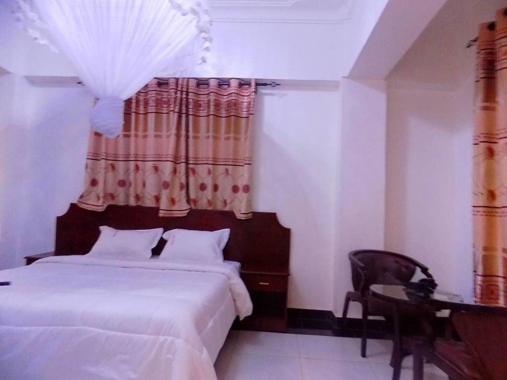 A bedroom with a bed, a nightstand, a chair, and a window with curtains.