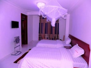 Ein Hotelzimmer mit zwei Betten, einem Deckenventilator, einem Fernseher und einem Fenster mit Vorhängen.