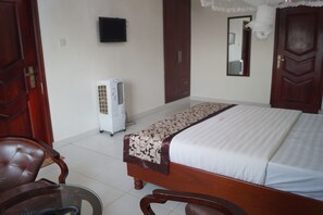 A bedroom with a bed, a chair, a heater, and a mirror on the wall. - Sunrise Hotel (Kampala)