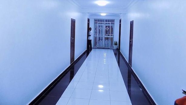A long, narrow hallway with white walls and a shiny floor, leading to a gated entrance. - Sunrise Hotel (Kampala)