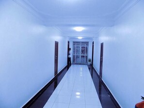 Um corredor comprido e estreito, com paredes brancas e chão brilhante, que leva a um portão de entrada.