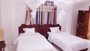 A room with two single beds, a wooden headboard, and a curtain with a striped pattern. - Sunrise Hotel (Kampala)