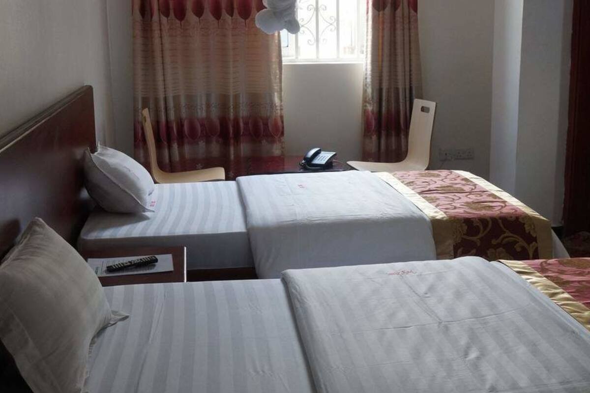 A hotel room with two single beds, a bedside table with a phone, and a window with curtains.