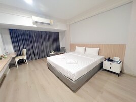 Una habitación de hotel con una cama, un escritorio, una silla, una mesita de noche y un aire acondicionado.