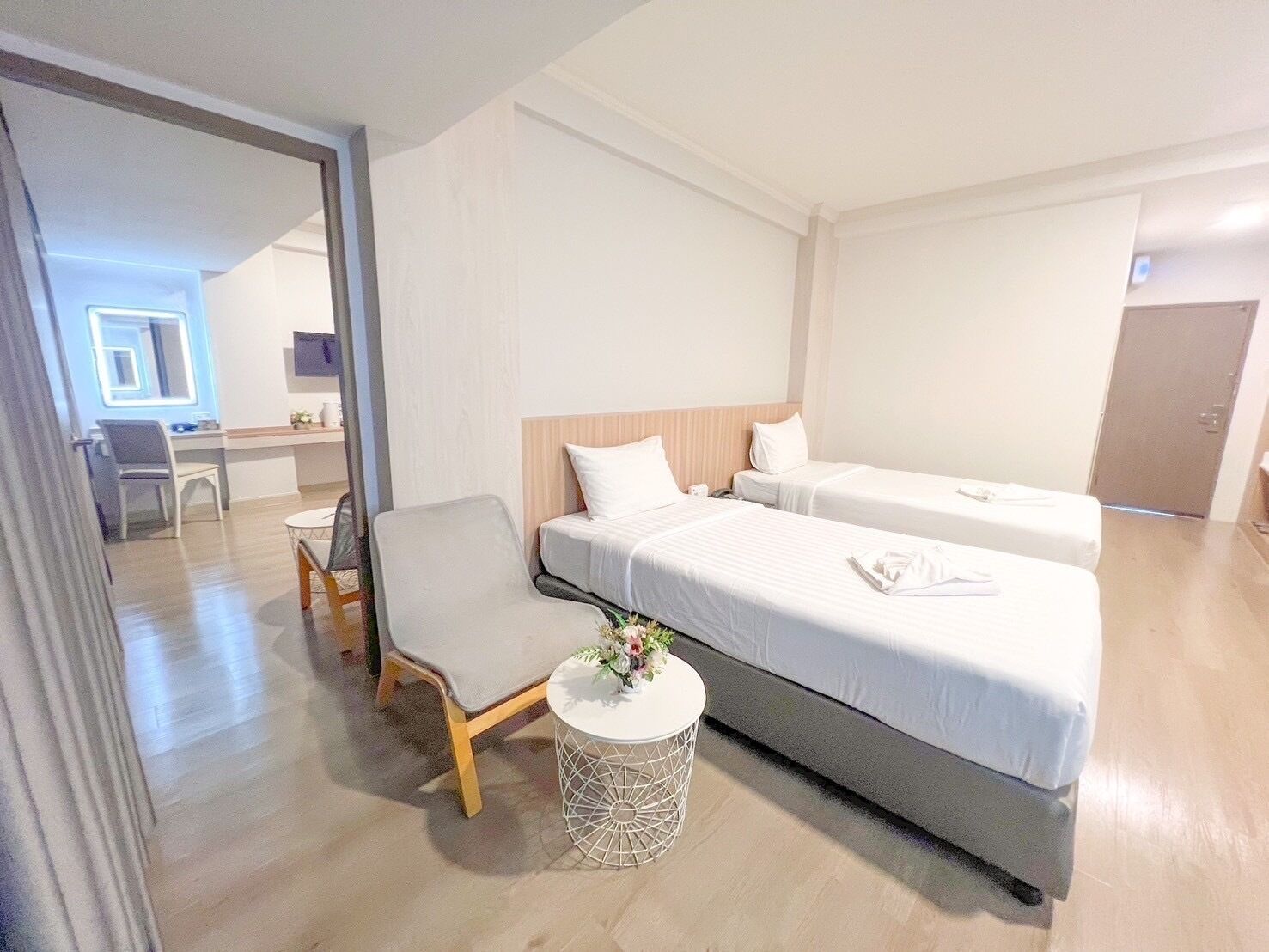Ein Hotelzimmer mit zwei Betten, einem kleinen runden Tisch mit einer Blume, einem Stuhl und einem Schreibtisch mit ebenfalls einem Stuhl.